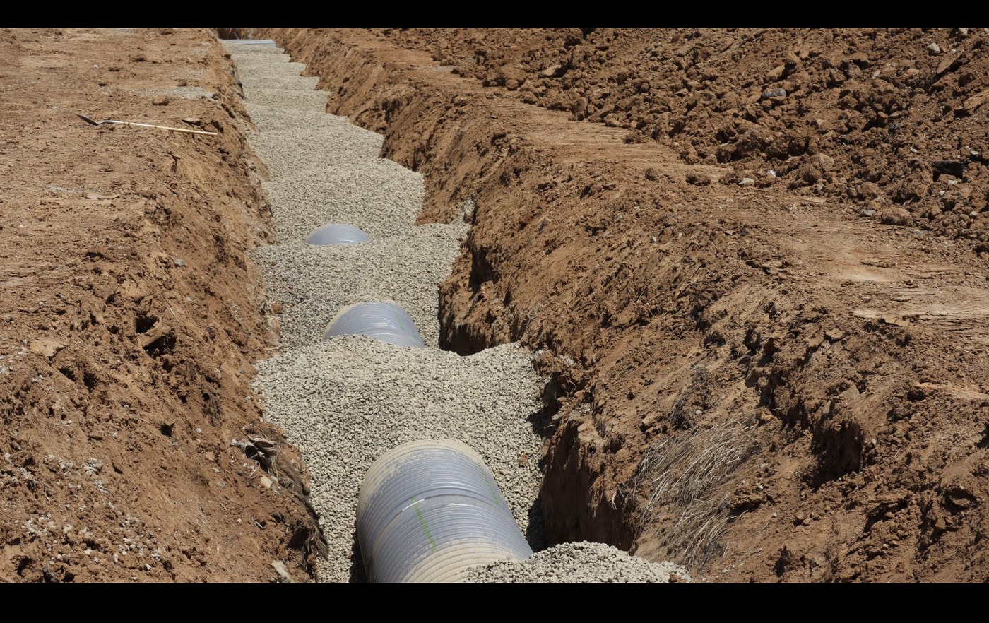 Open trench with bedding stone and drainage pipe during an excavation
