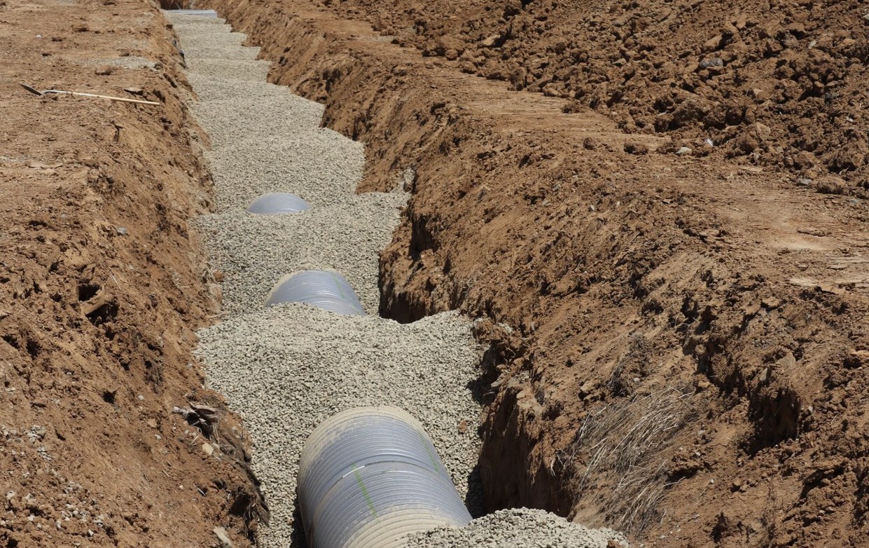 Open trench with bedding stone and drainage pipe during an excavation